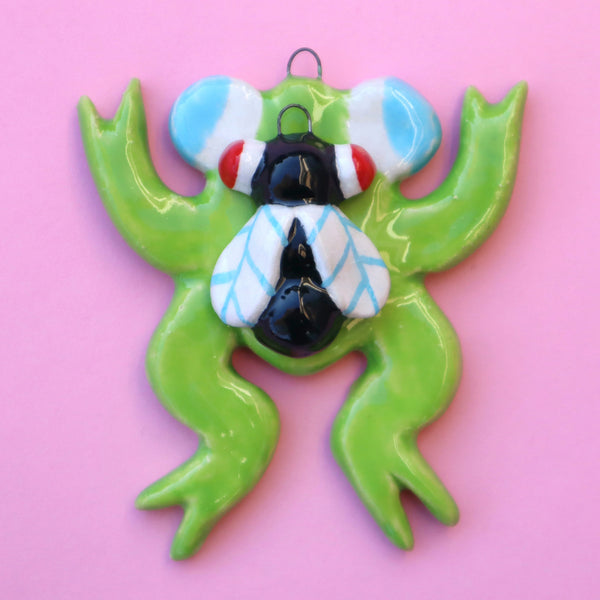 Ceramic Frog and Fly Holiday Ornaments spread out across a Pink Background made by Eva Stalinski 2022