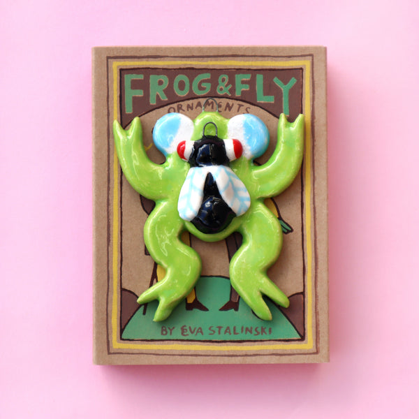 Ceramic Frog and Fly Holiday Ornaments with hand printed kraft paper matchbox on a Pink Background made by Eva Stalinski 2022